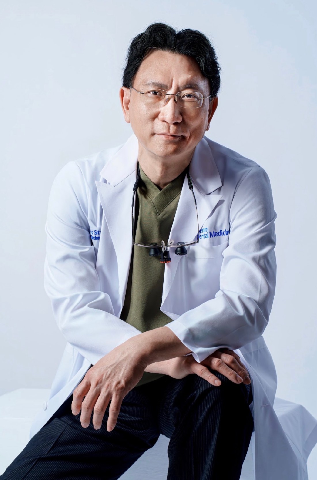 Dr. Steven Liu, DMD, DDS, periodontist, seated in his Penn Dental Medicine coat with surgical loupes